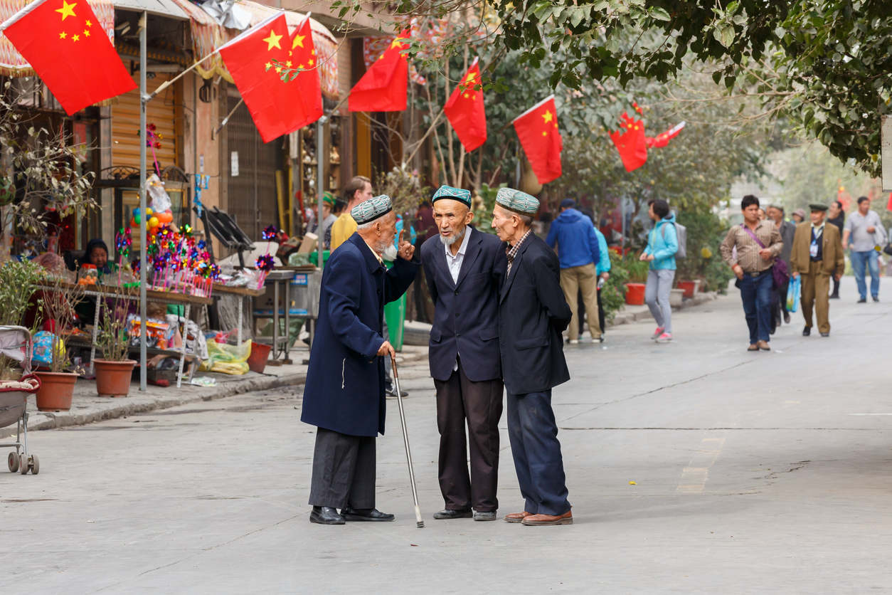 Three elderly Uighur men having a conversation in front of Chinese flags