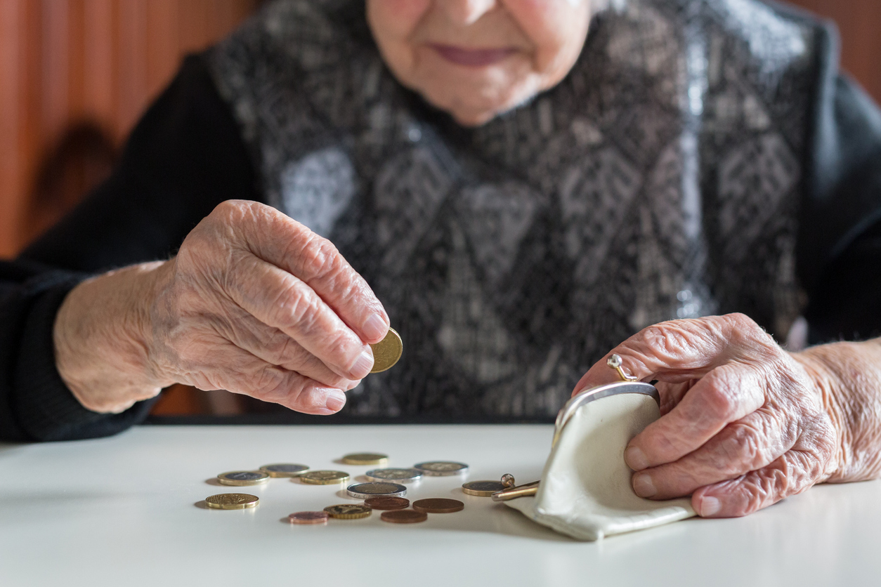 Elderly woman sitting at the table counting money in her wallet