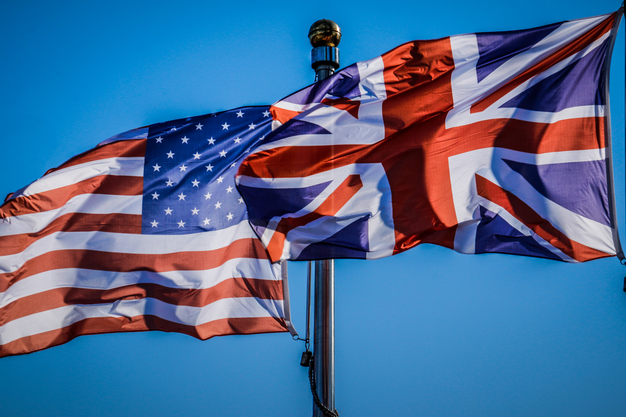 US and UK flag against blue sky