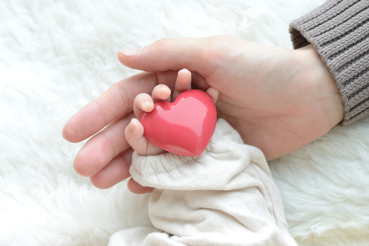 Baby's hand with heart object and mother's hand