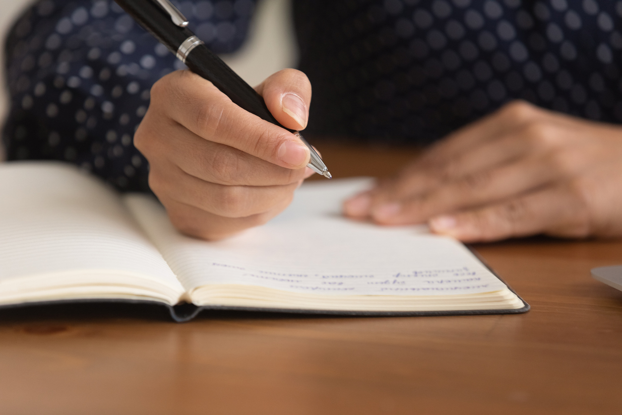 Close up woman taking notes in notebook, holding pen