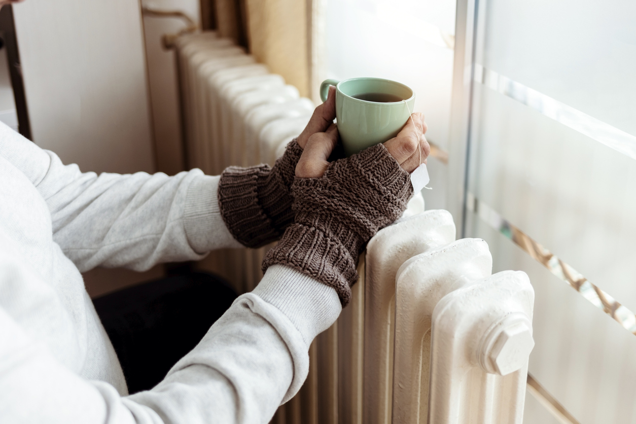 Elderly person warming their hands on a radiator.