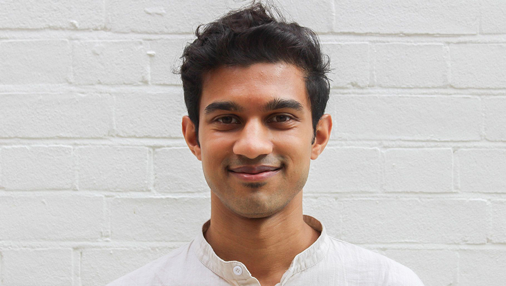 Young legal tech professional standing in front of white brick wall.