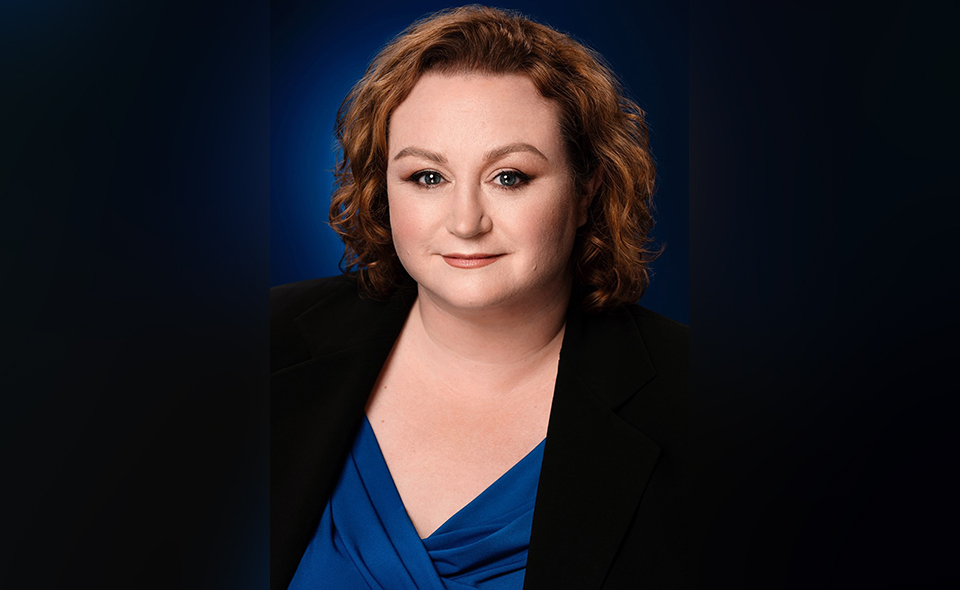 Female general counsel in business attire standing in front of a black background.