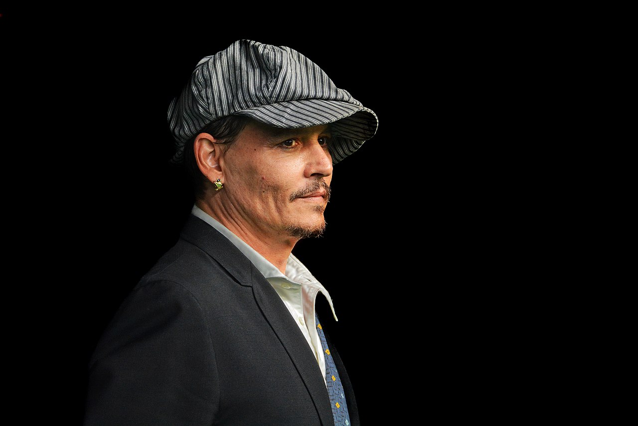 Johnny Depp wearing flat cap against a black background.