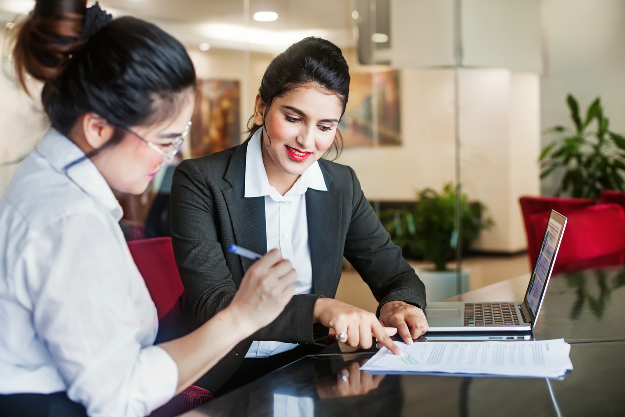 Two female legal counsel looking at a laptop and paper notes.