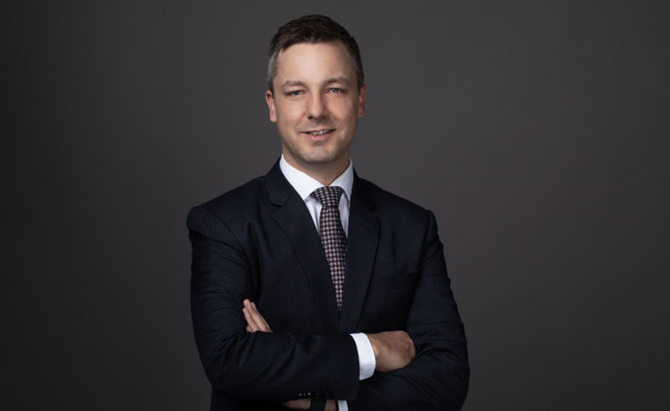 Swiss lawyer in formal suit standing in front of dark background.