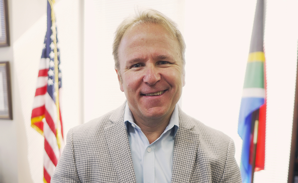 US immigration expert Leon Versfeld standing in front of flags.