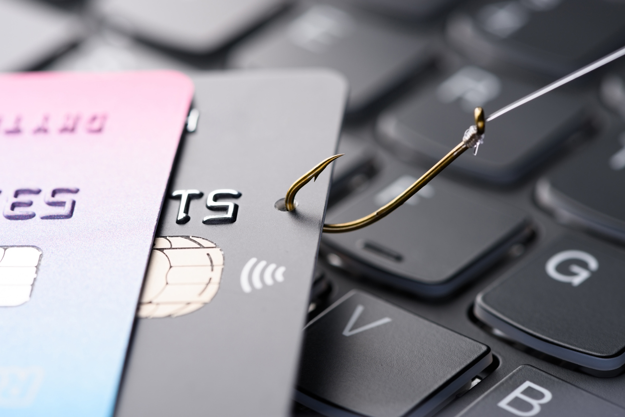 Credit card on fishing hook pulled from stack on keyboard, phishing scam data theft concept