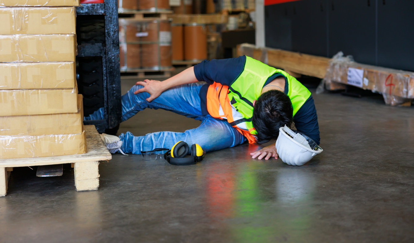 First Aid and safety first concept. Warehouse man worker lying down on floor after accident in warehouse factory. Professional engineering teamwork. Health insurance emergency accident in workplace.