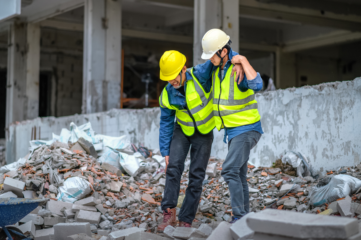 Construction supervisors or engineers help construction workers who have knee and leg injuries, caused by accidents at the construction site.