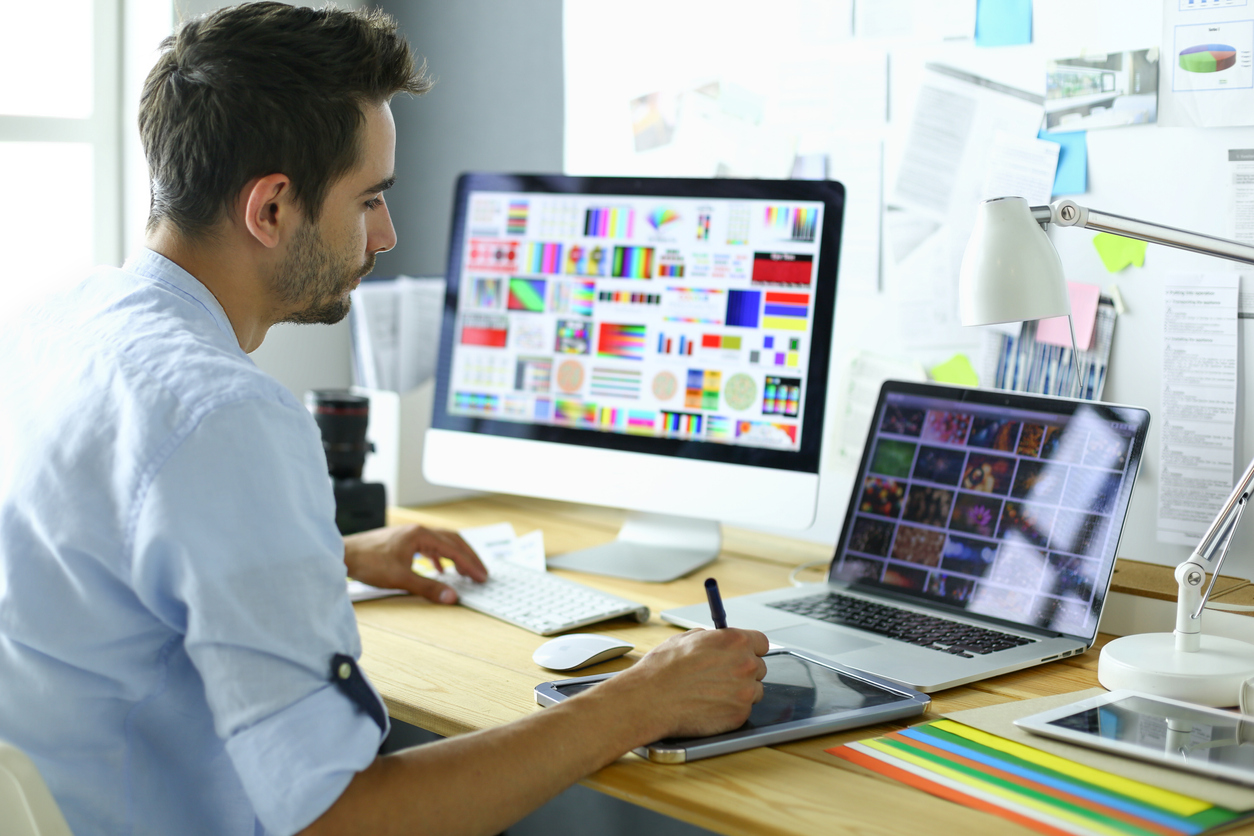 Portrait of young designer sitting at graphic studio in front of laptop and computer while working online