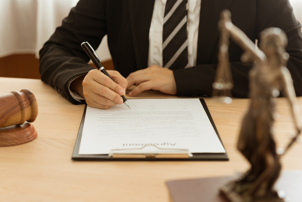 lawyer signing contract document with judge gaval, scales of justice on desk in law office.