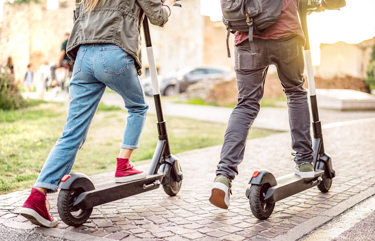 millenial couple riding electric scooters at urban city park genz students using new ecological mean of transportation green eco energy concept with zero emission warm filter with sunshine halo