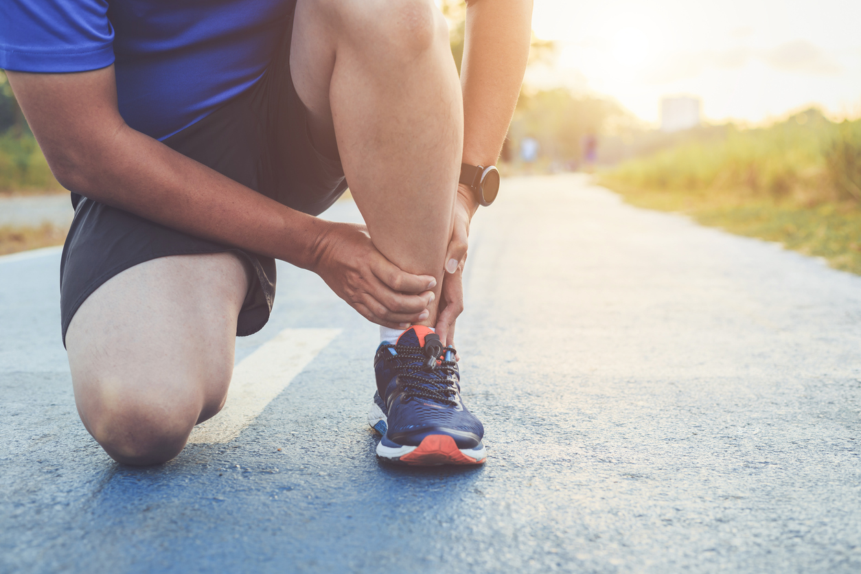 injury from workout concept : asian man use hands hold on his ankle while running on road in the park. focus on ankle.