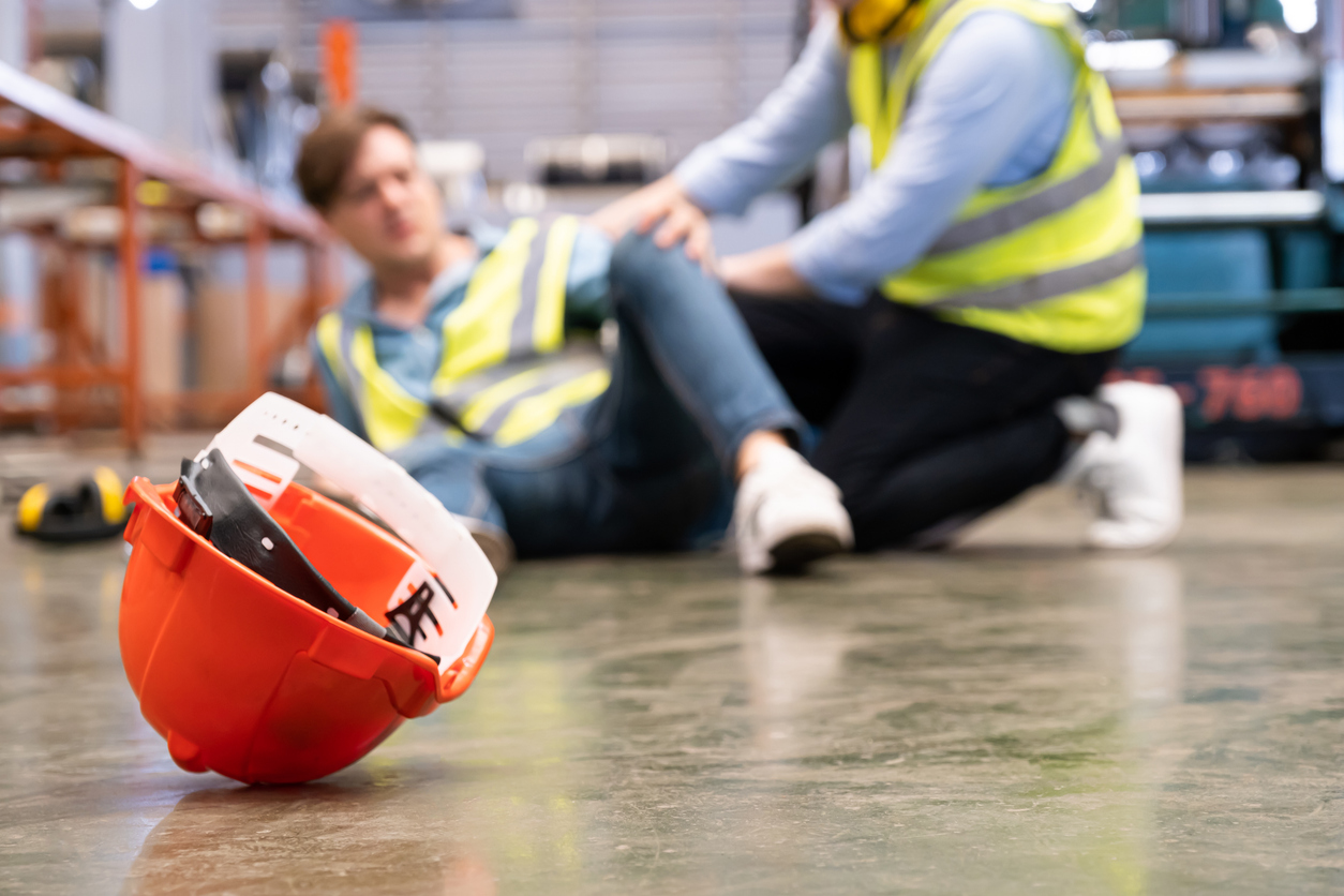 selective focus at hat, men worker feel painful and hurt from the accident that happen inside of industrial factory while his co worker come to give emergency assistance and help. accident in factory.