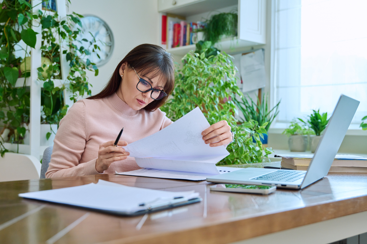 middle aged woman working remotely in home office, at workplace with computer