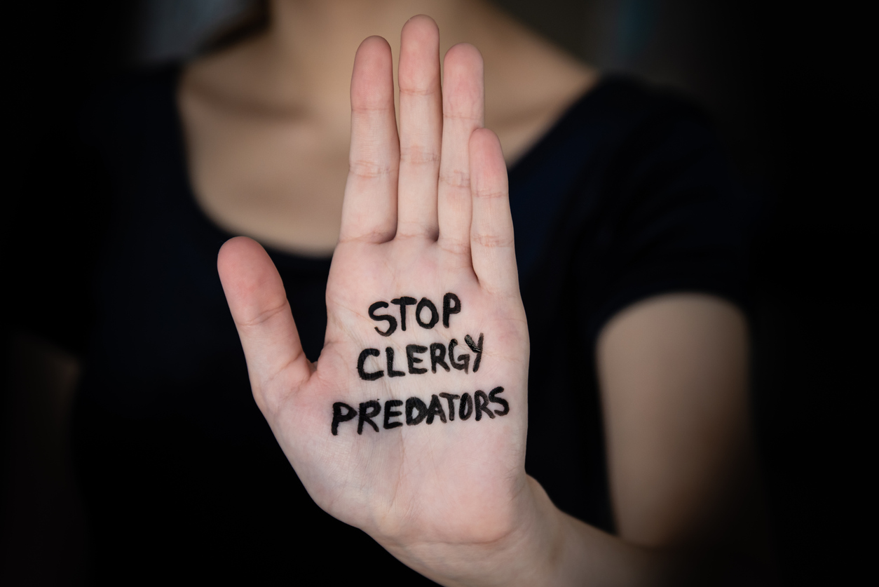 woman's hand held out with open palm with words stop clergy abuse written on hand