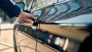 cropped photo of a male hand opening the door of a black car while standing outdoors