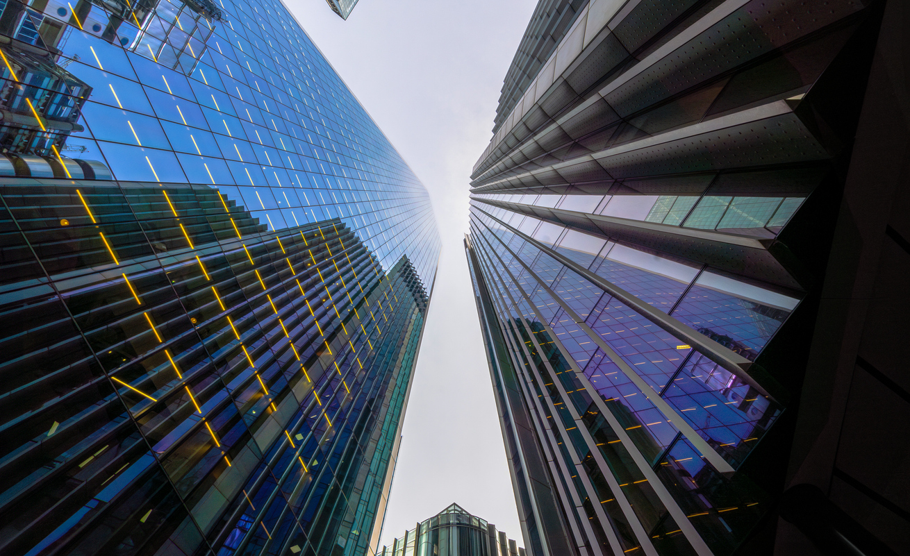 two modern skyscrapers with glass facades seen in perspective from below in nadir plane under a white sky.