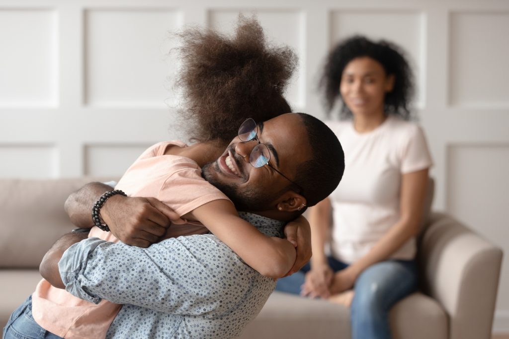 happy african american dad embracing daughter cuddling at home