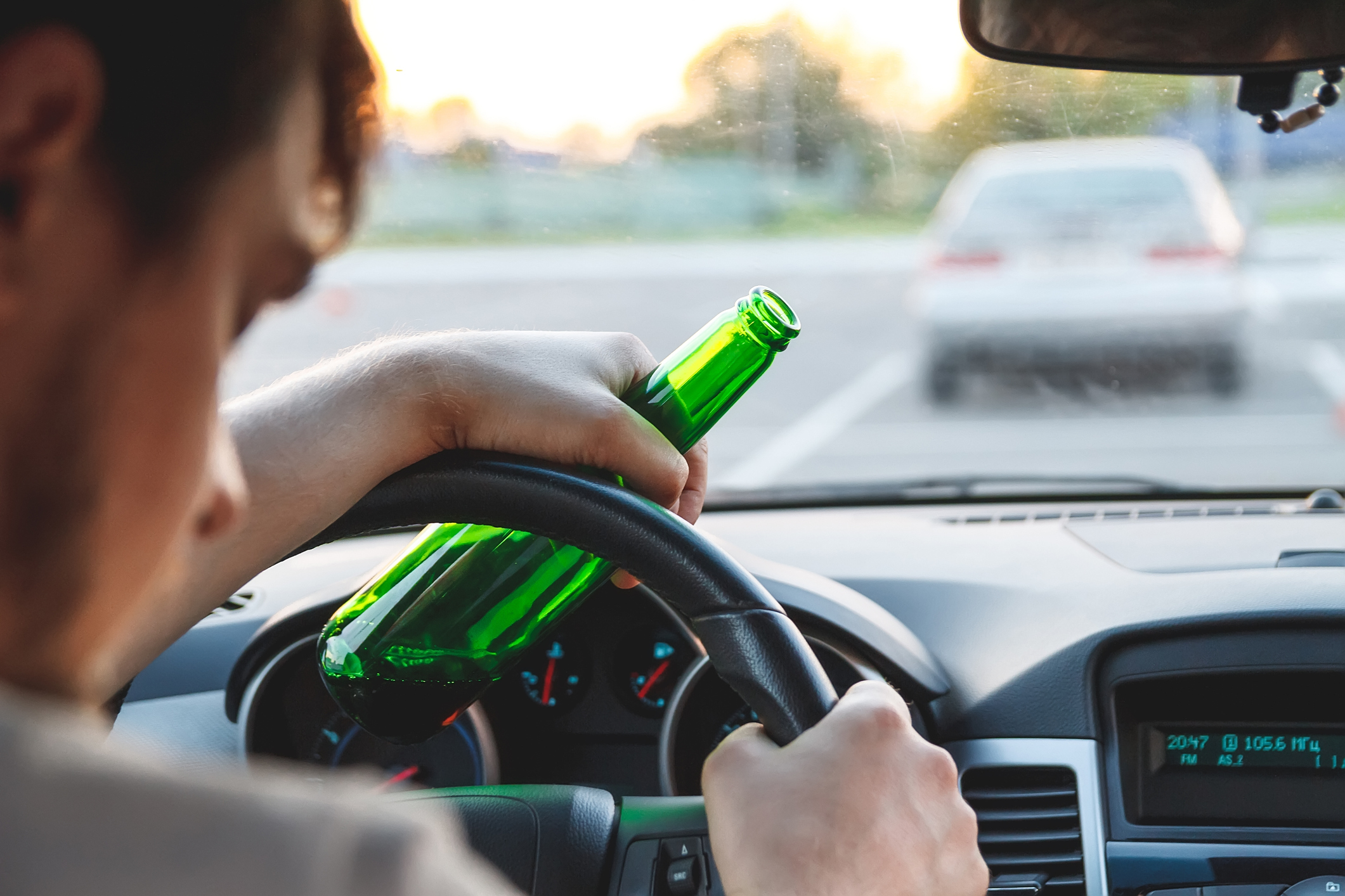 a man driving a car with a bottle of beer