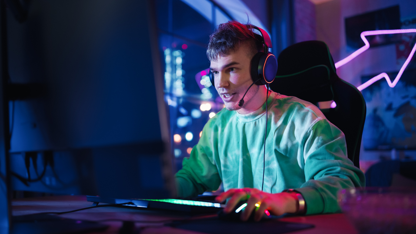 gaming at home: portrait of a gamer wearing headphones and playing online game on personal computer. professional stylish male player enjoying online multiplayer pvp tournament.