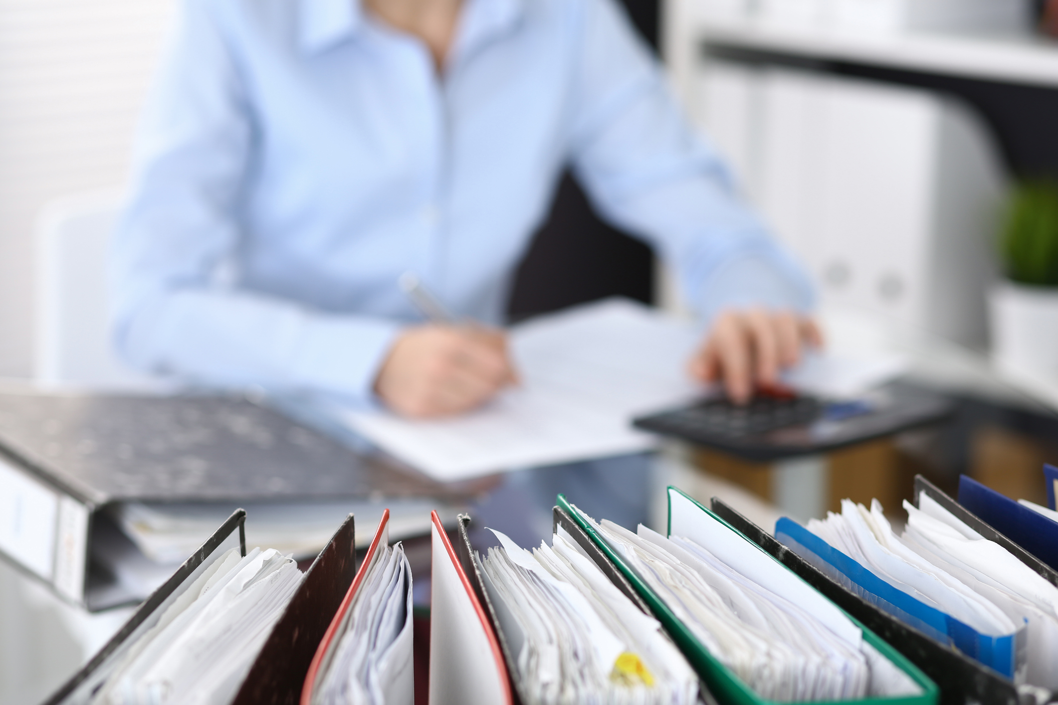 binders with papers are waiting to be processed with businesswoman or secretary back in blur