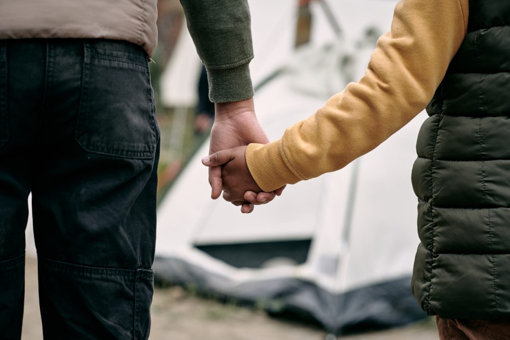 holding hand of child against migrant camp