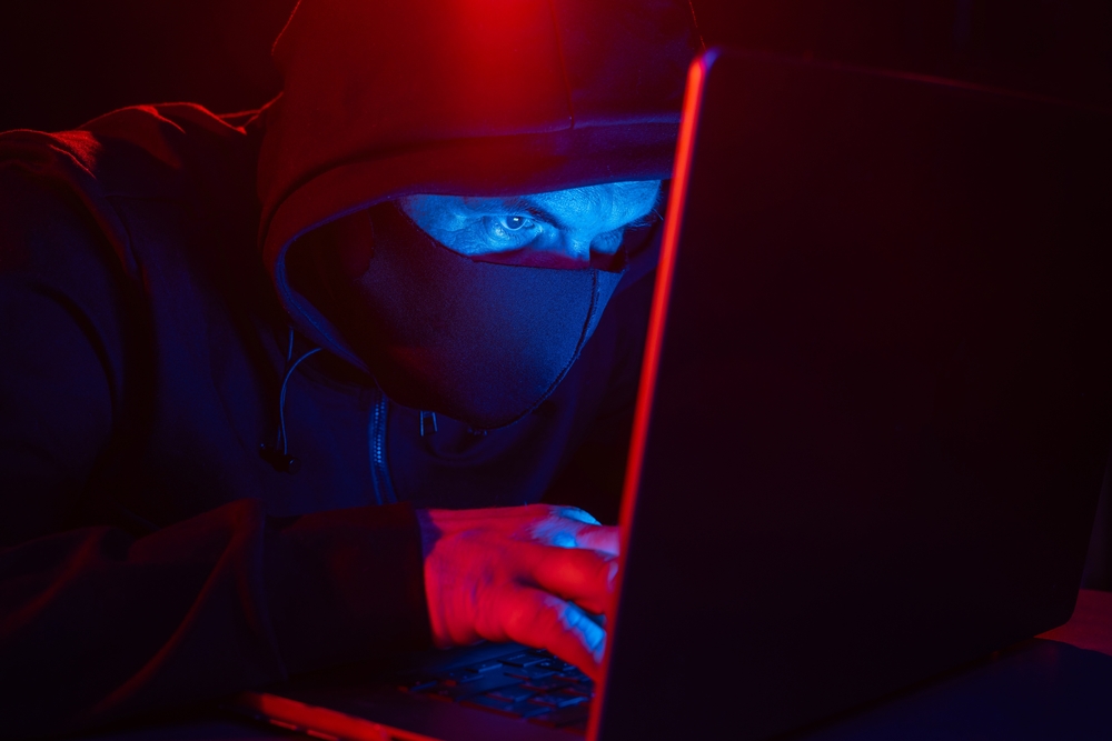 cyber,hacker,in,hood,behind,laptop,on,dark,background,with