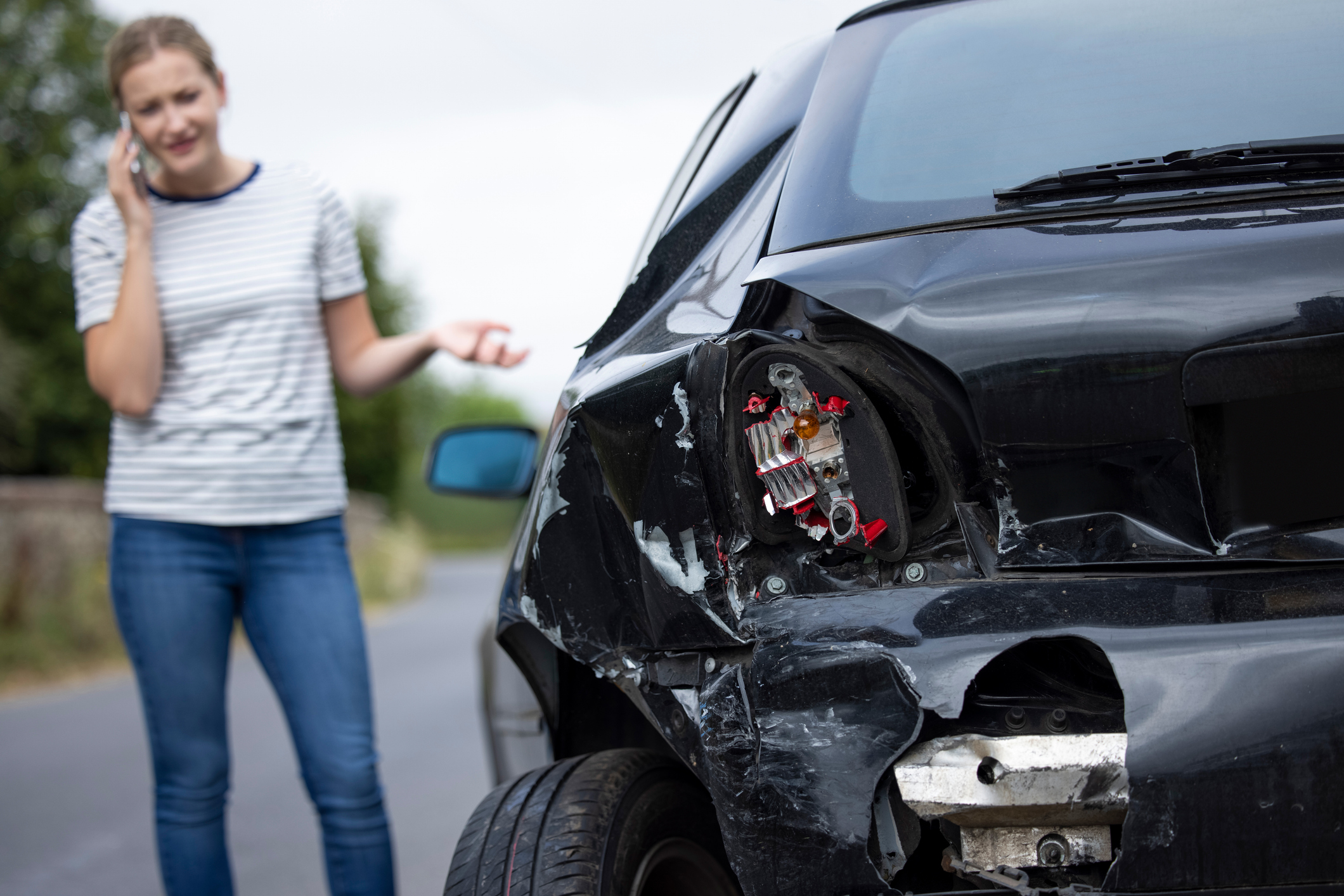 unhappy female driver with damaged car after accident calling insurance company on mobile phone