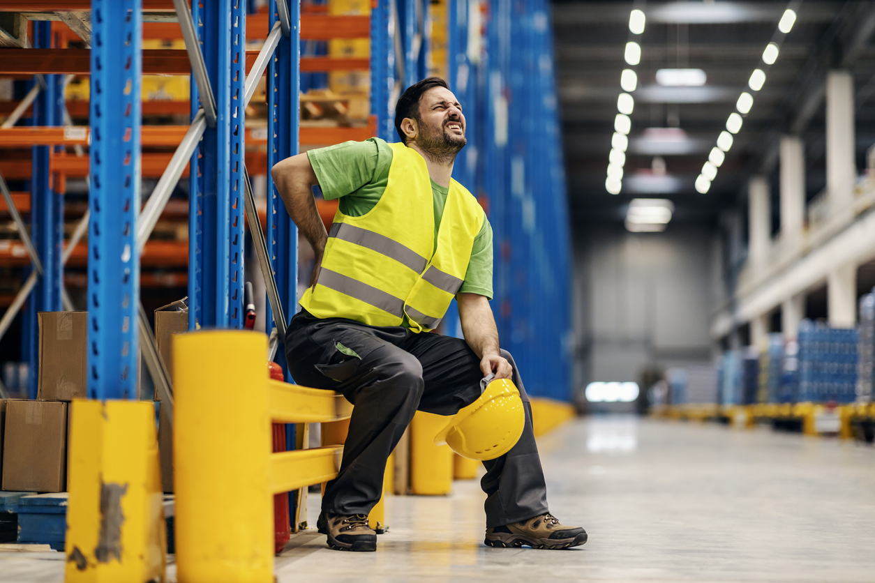 a warehouse worker having back pain and rubbing it.