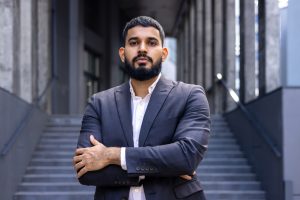 portrait of a young muslim male lawyer standing in a business suit outside a courthouse and looking confidently into the camera with his arms crossed