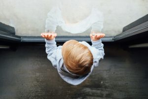 blonde haired boy in grey top leaning on glass door